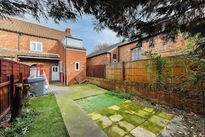 A backyard with a paved area, a grassy lawn, and a brick house. - Modern 2-BR Cottage with Private Entrance (Newark-on-Trent)