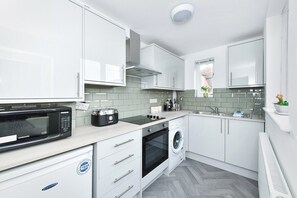 A modern kitchen with white cabinets, a microwave, a toaster, a washing machine, and a window with a view of greenery.