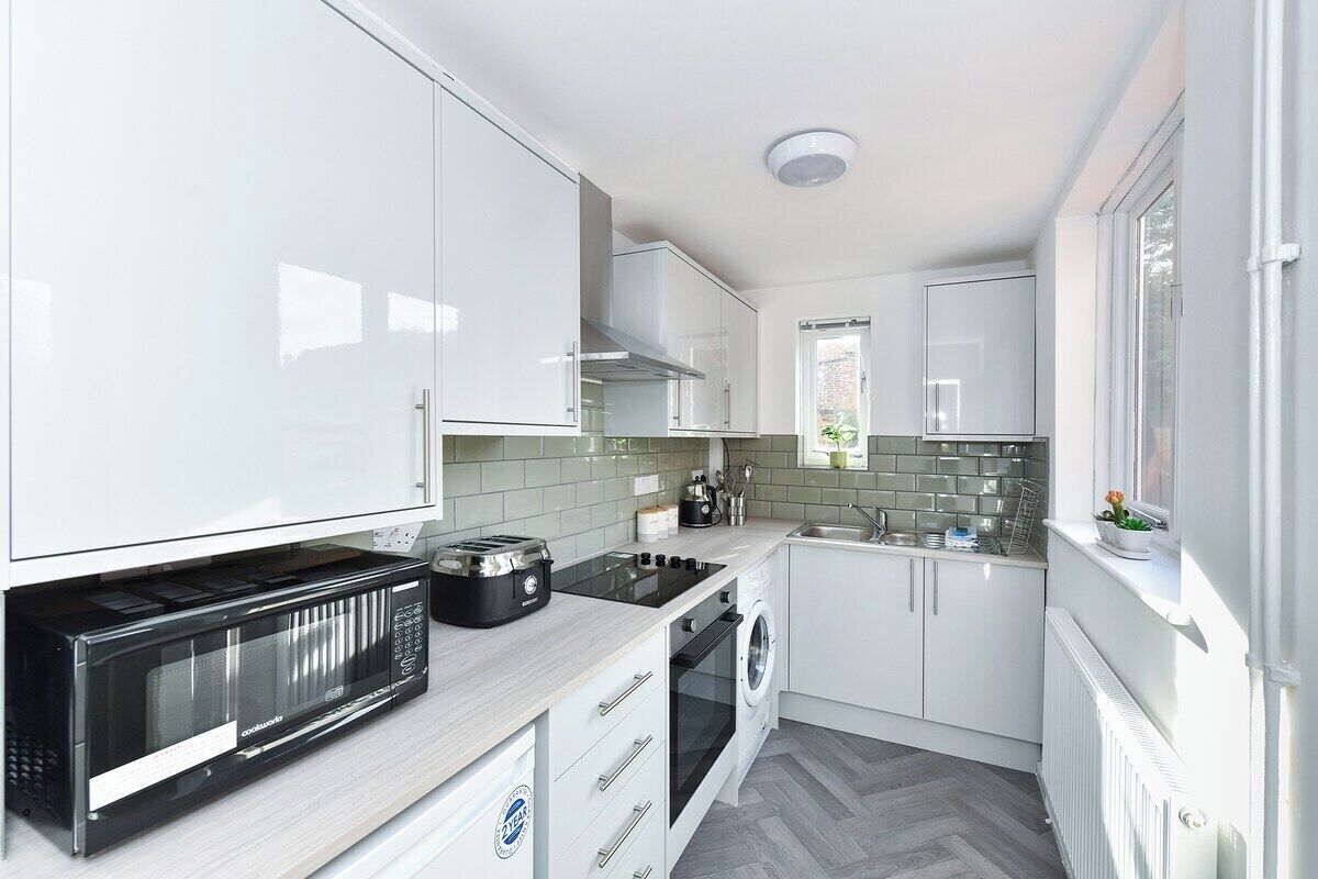 A modern kitchen with white cabinetry, a built-in microwave, a stove, and a washing machine.