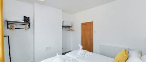 Una habitación de hotel con cama, armario, radiador y estante con toallas.
