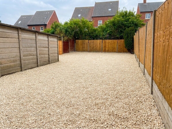 A gravel-covered backyard with wooden fences and a brick house in the background. - 3-Bed House w/ Driveway Parking (Nottingham)