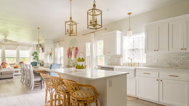 Una cocina amplia con muebles blancos, una isla grande con taburetes y lámparas colgantes.