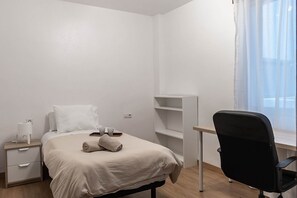 Une chambre à coucher au style minimaliste, comprenant un lit, une table de chevet et un bureau avec une chaise.