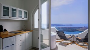 A modern kitchen with a wooden countertop, white cabinets, and a view of a scenic landscape through a large window. - Aethria Suite with Caldera view (Santorini)