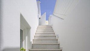 A narrow staircase leading up to a door, surrounded by white walls and a clear blue sky. - Aethria Suite with Caldera view (Santorini)