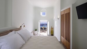 A bedroom with a bed, a bedside table, a lamp, a plant, and a view of the outdoors. - Aethria Suite with Caldera view (Santorini)