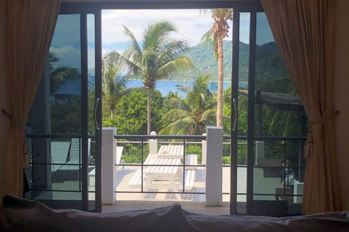A room with a large window offering a view of palm trees and a body of water.