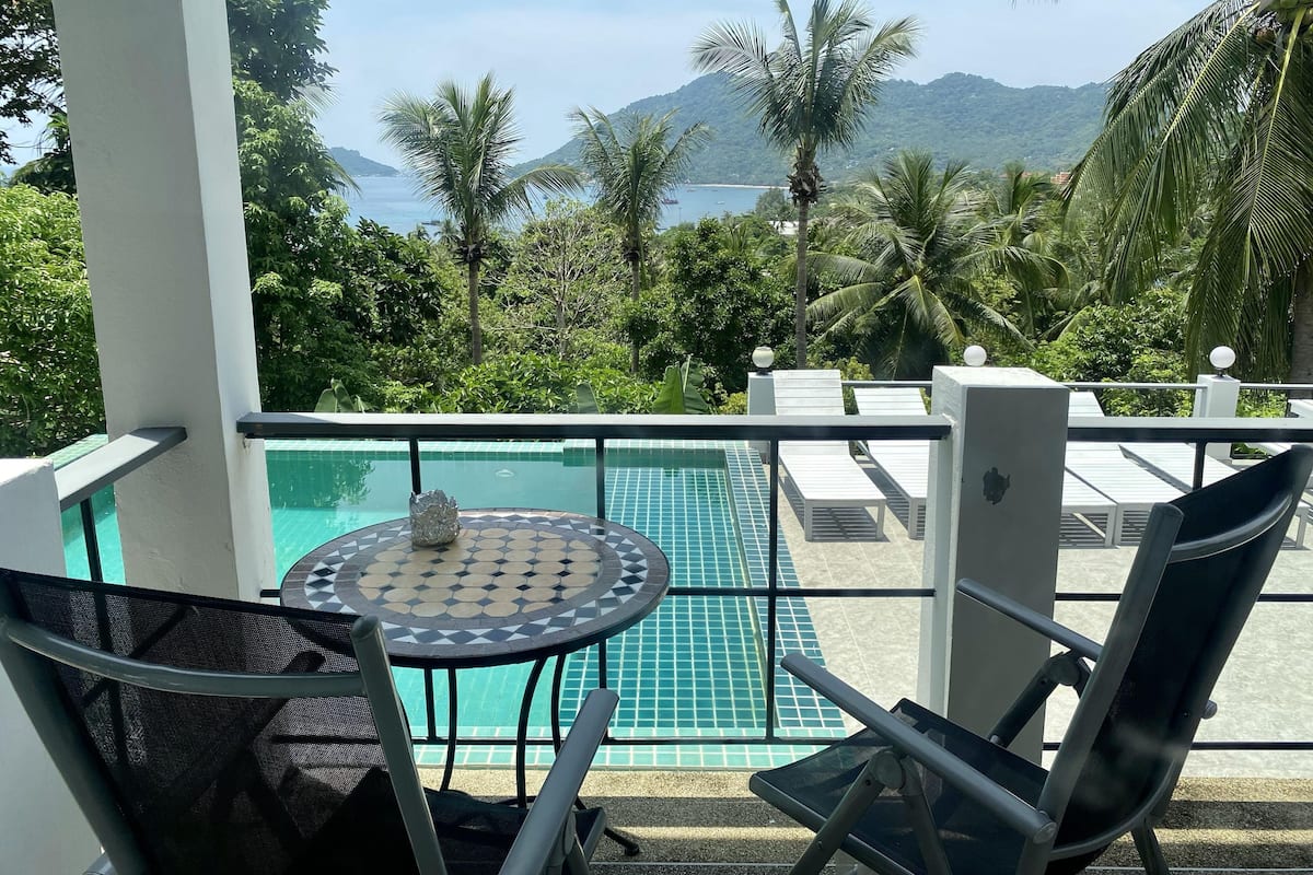 A balcony with a view of a pool, palm trees, and mountains.