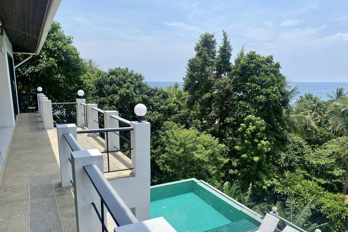 A rooftop pool with a view of the ocean, surrounded by lush greenery.