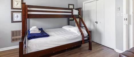 A bunk bed with a ladder, white bedding, and a blue towel. There is a white door and a vent on the wall.