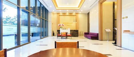 A spacious lobby with a large wooden table, a reception desk, and a purple sofa.