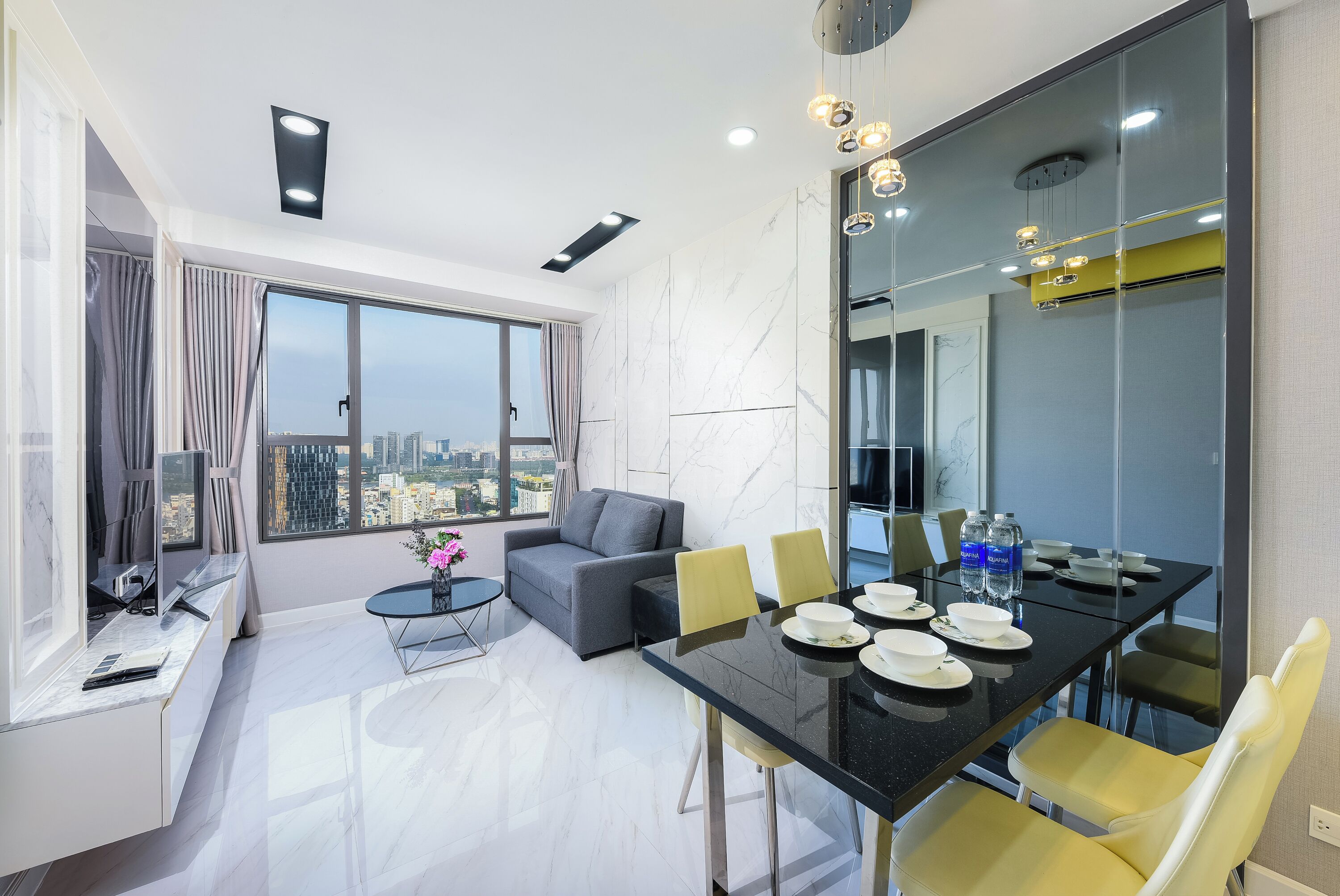 Uma sala de estar moderna com sofá, mesa de jantar e cadeiras. Há uma janela grande com vista para a cidade.