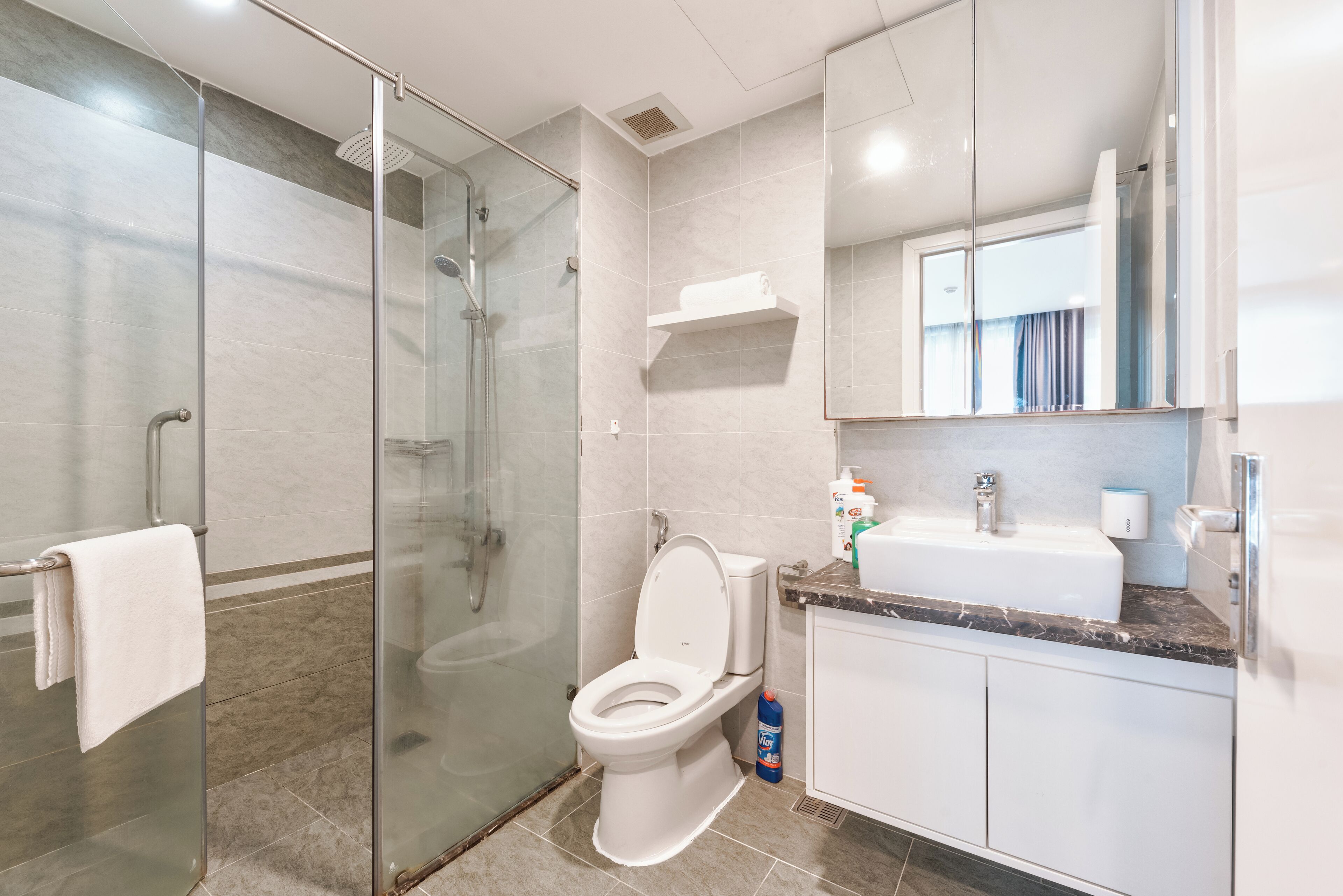 Et moderne badeværelse med en brusekabine i glas, et hvidt toilet, en marmorplade og et stort spejl.