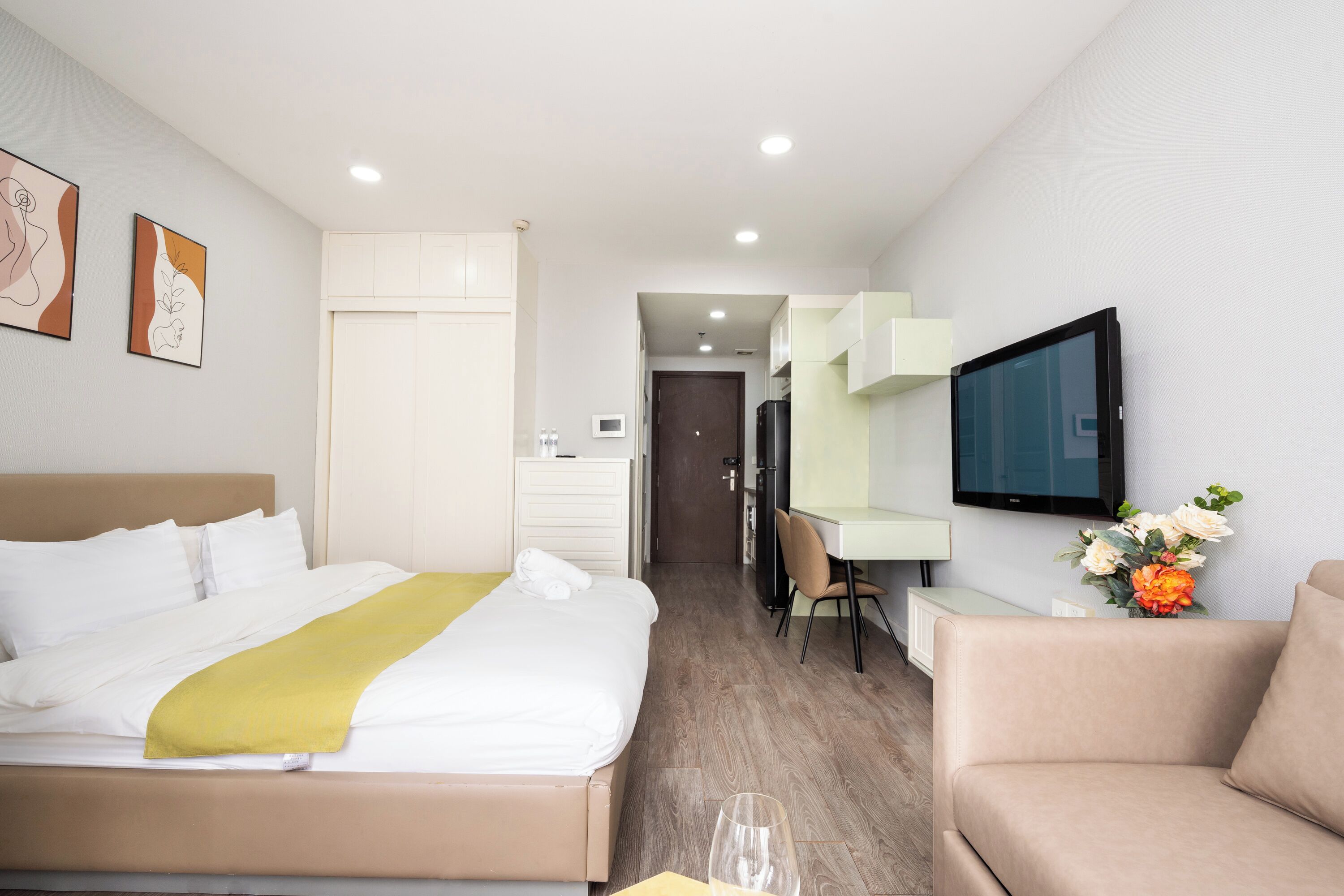 A hotel room with a bed, a desk, a chair, a TV, and a flower arrangement.