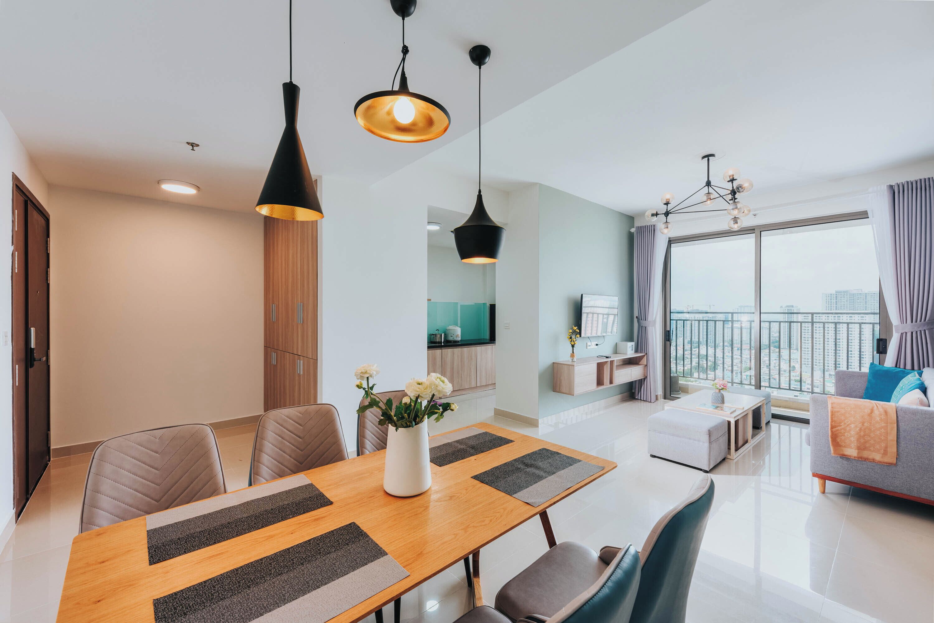 A modern living room with a dining area, large windows with curtains, and a view of the city.