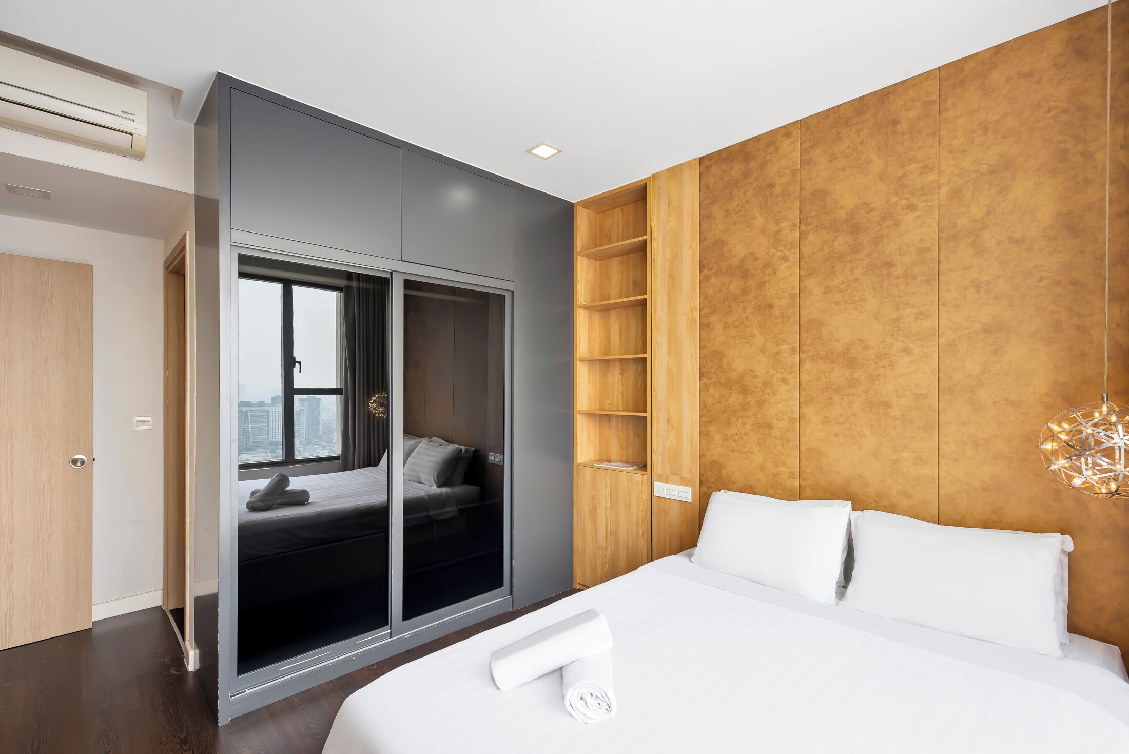 A modern hotel room with a large bed, a sliding door closet, a wooden panel wall, and a city view.