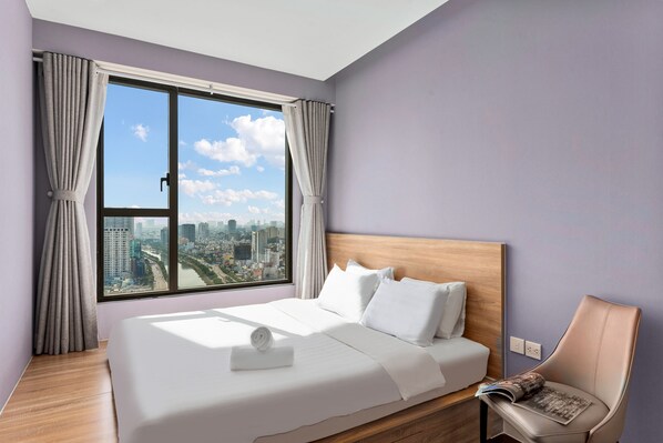 A modern hotel room with a large bed, a view of the city, and a wooden headboard. - REM Rivergate Garden Pool Signature Apartments (Ho Chi Minh City)