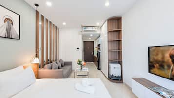 Una habitación de hotel moderna con una cama bien hecha, un sofá, una mesita con un jarrón de flores, un televisor y una estantería.