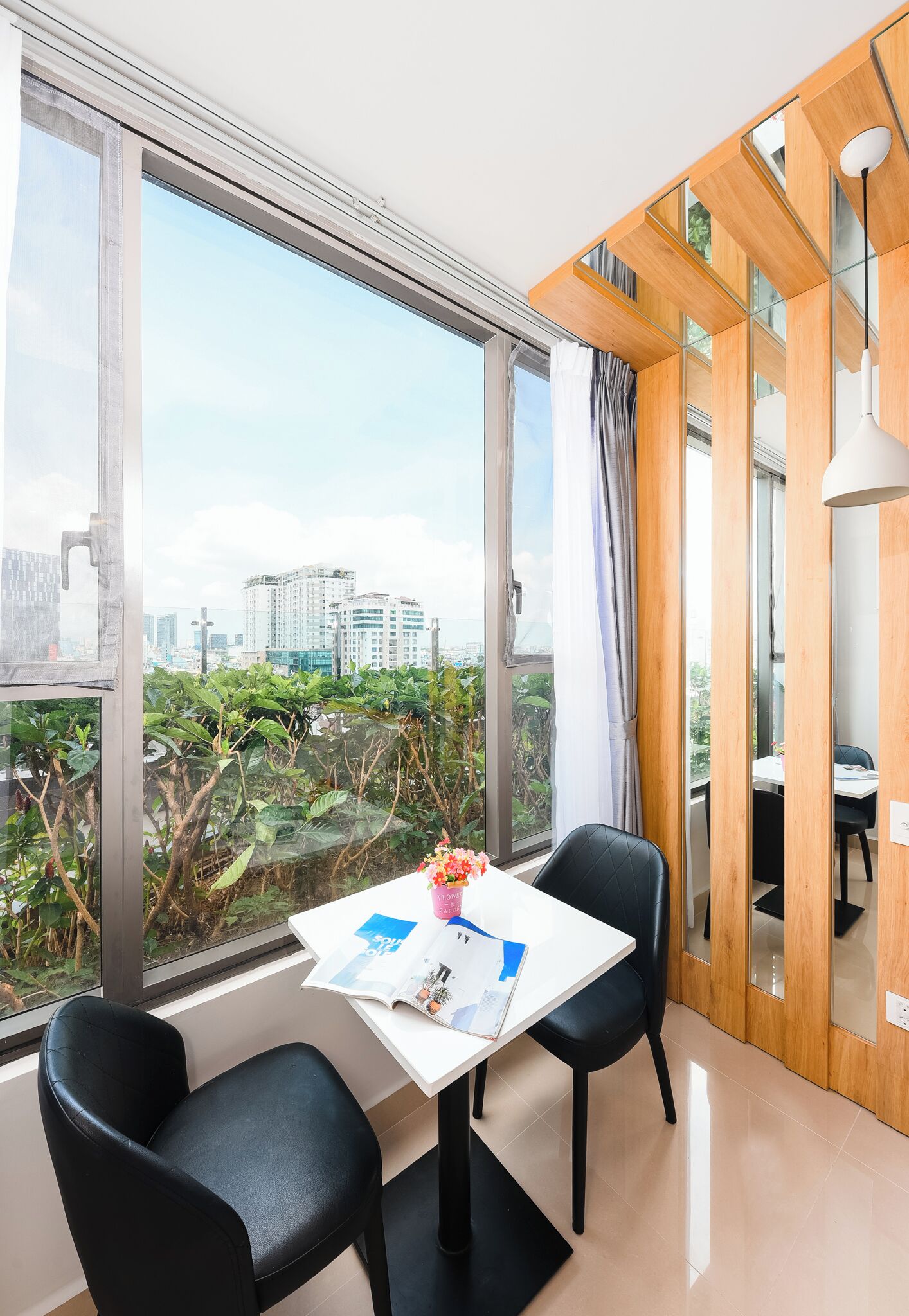 A modern room with a large window, a white table, two black chairs, and a wooden partition.