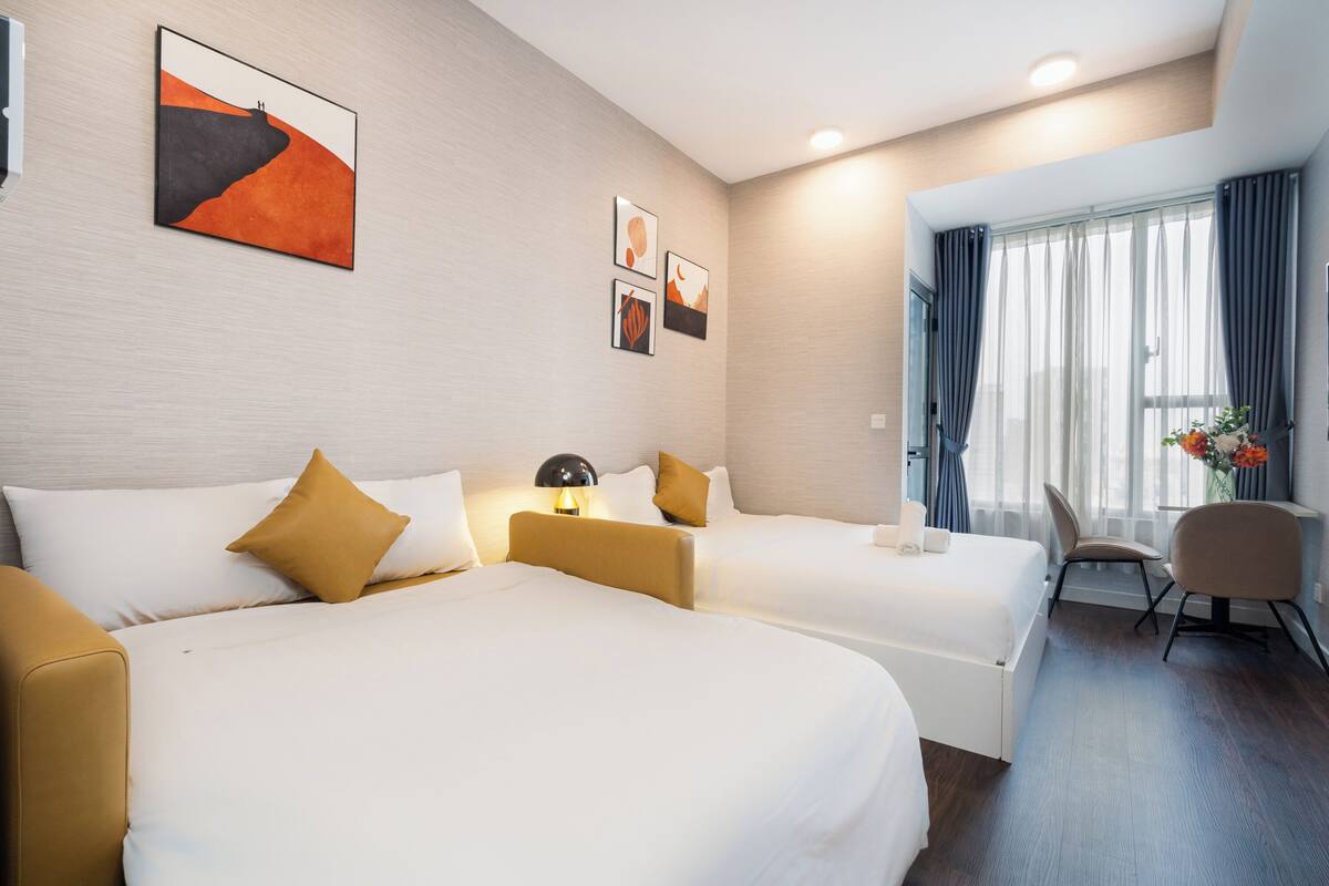 A hotel room with two beds, a desk, and a chair. There are three framed pictures on the wall.