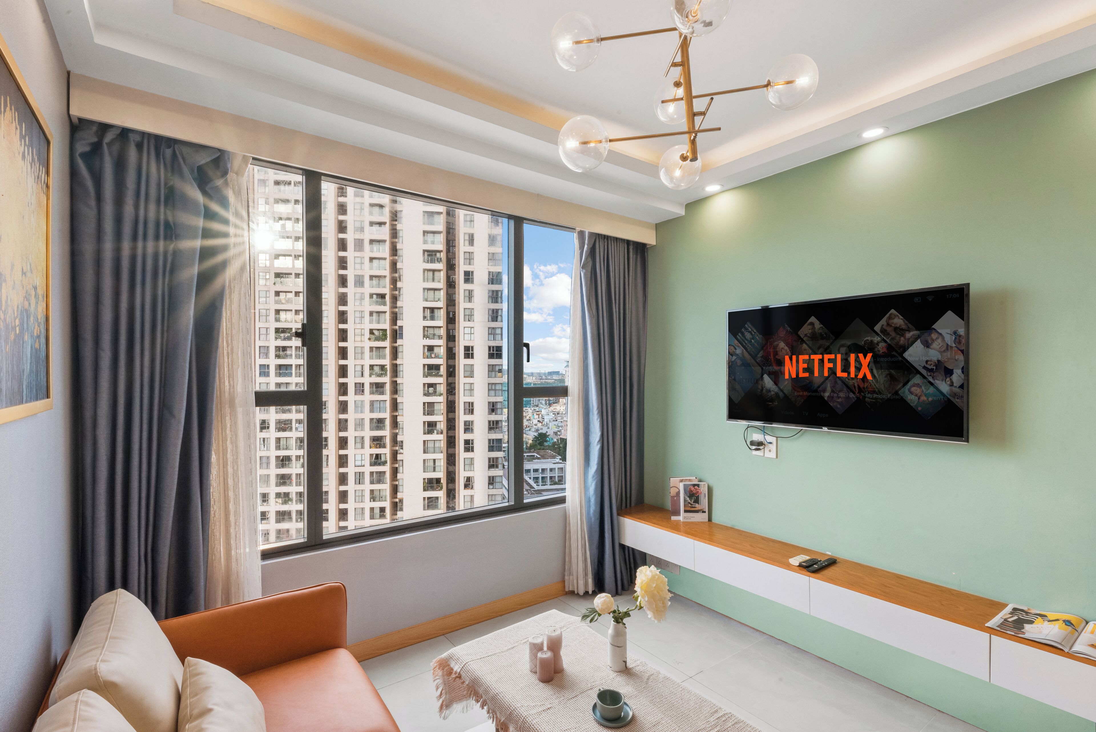 Una sala de estar moderna con un ventanal grande, un televisor de pantalla plana montado en la pared, un sofá, una mesita con velas y un jarrón decorativo.