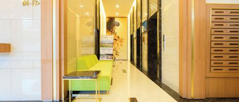 A modern lobby with a green sofa, a glass table, and a wooden cabinet with drawers.