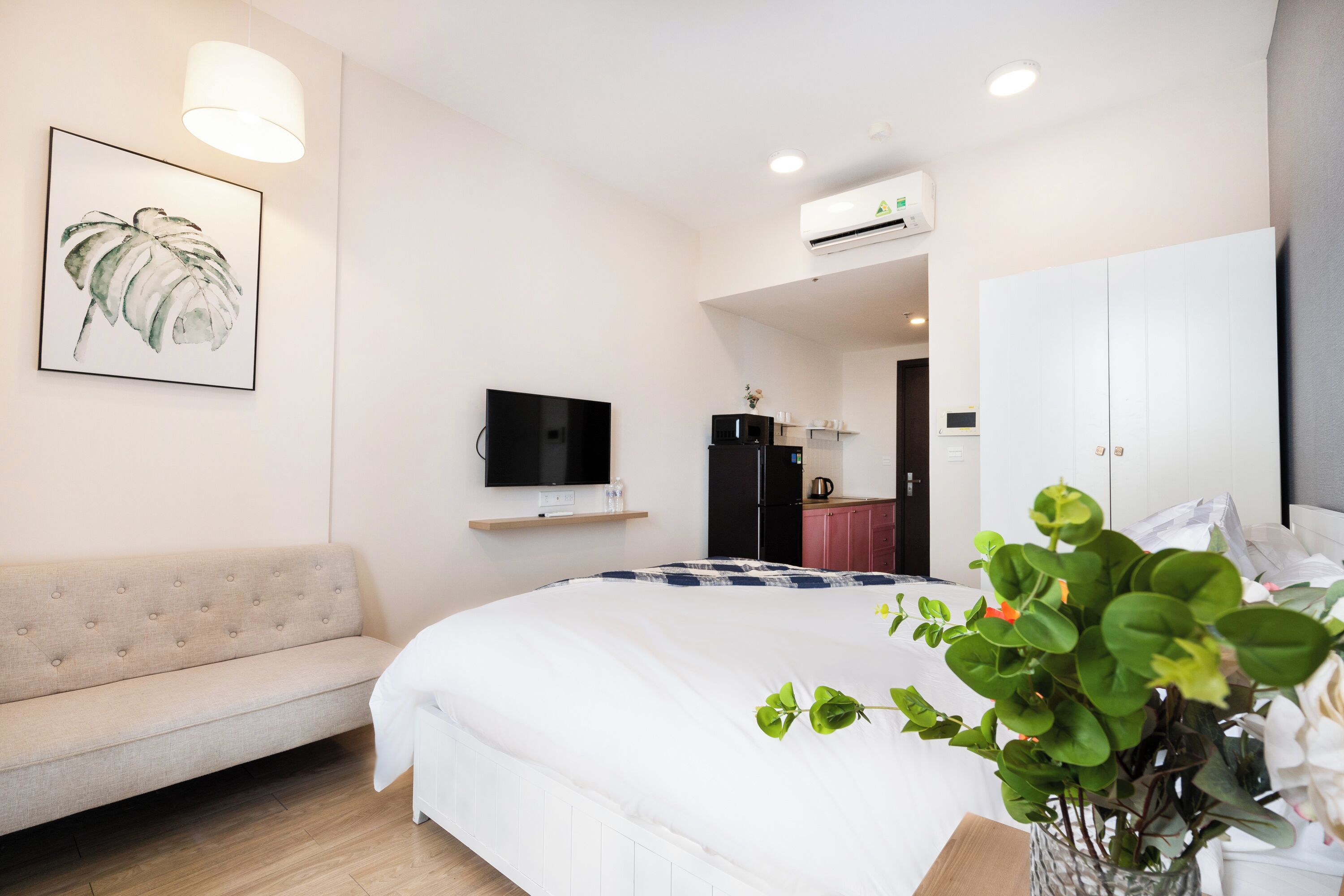 A modern hotel room with a large bed, a sofa, a TV, and a kitchenette.
