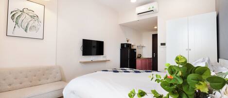A modern hotel room with a large bed, a sofa, a TV, and a kitchenette.