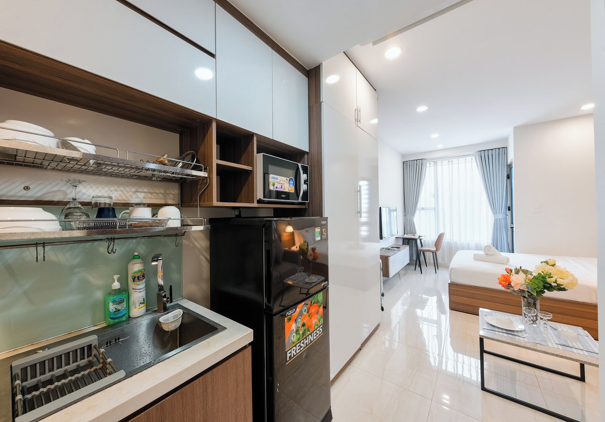 A modern hotel room with a kitchenette, a dining area, and a living space.