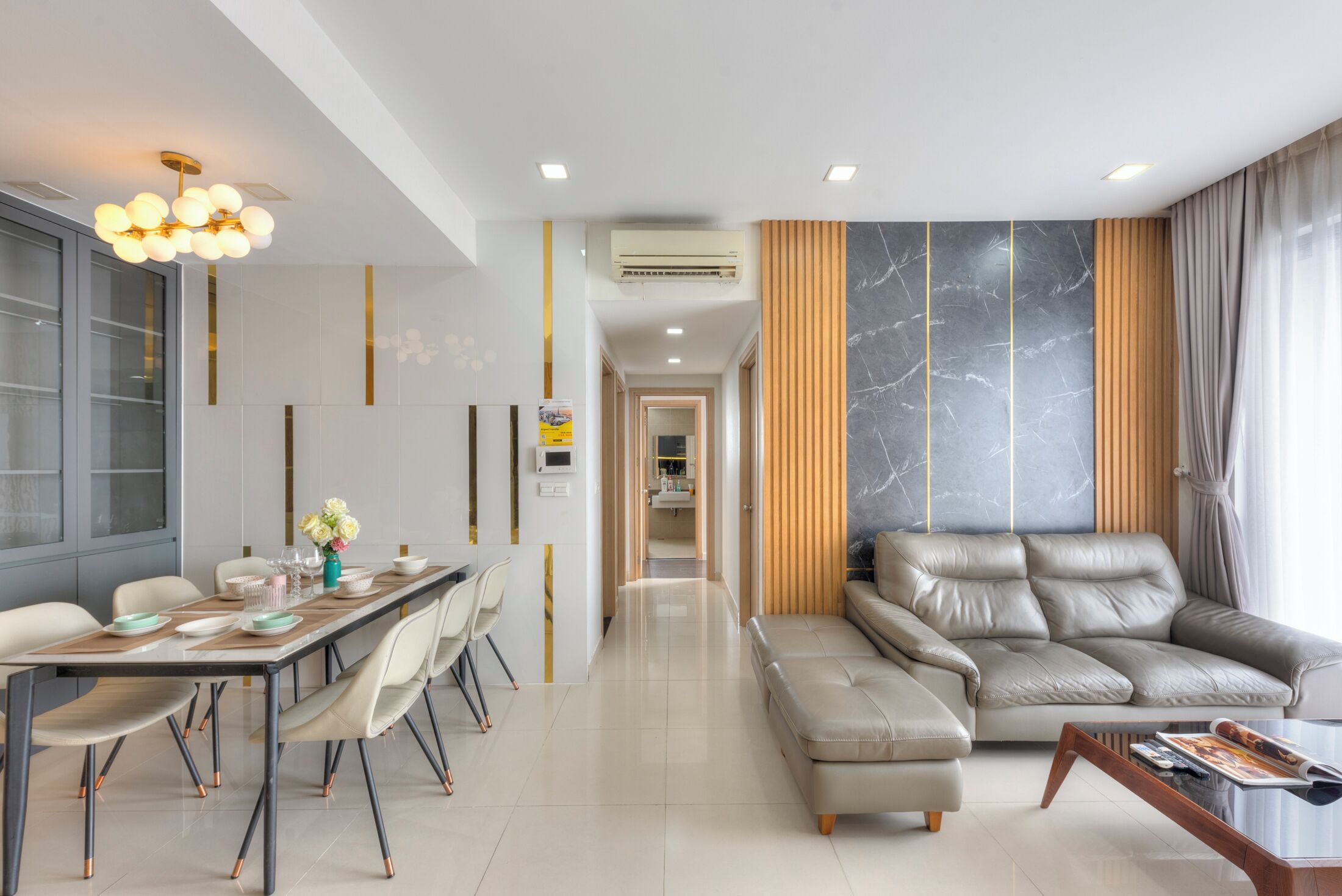 A modern living room with a sofa, a dining table with chairs, and a chandelier.