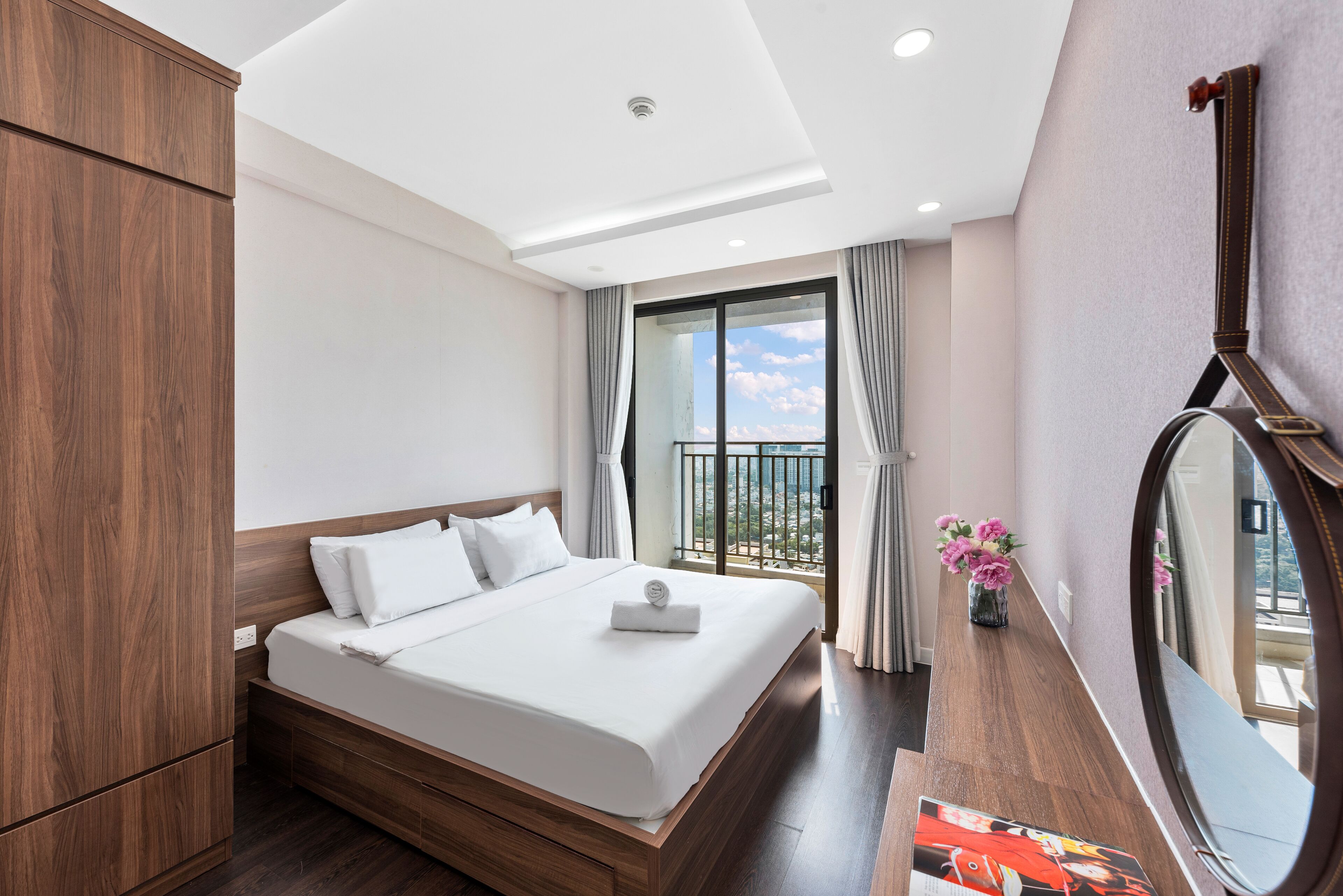 Une chambre d’hôtel avec un grand lit, une armoire en bois, une petite table ornée d’un vase de fleurs et un balcon avec vue.