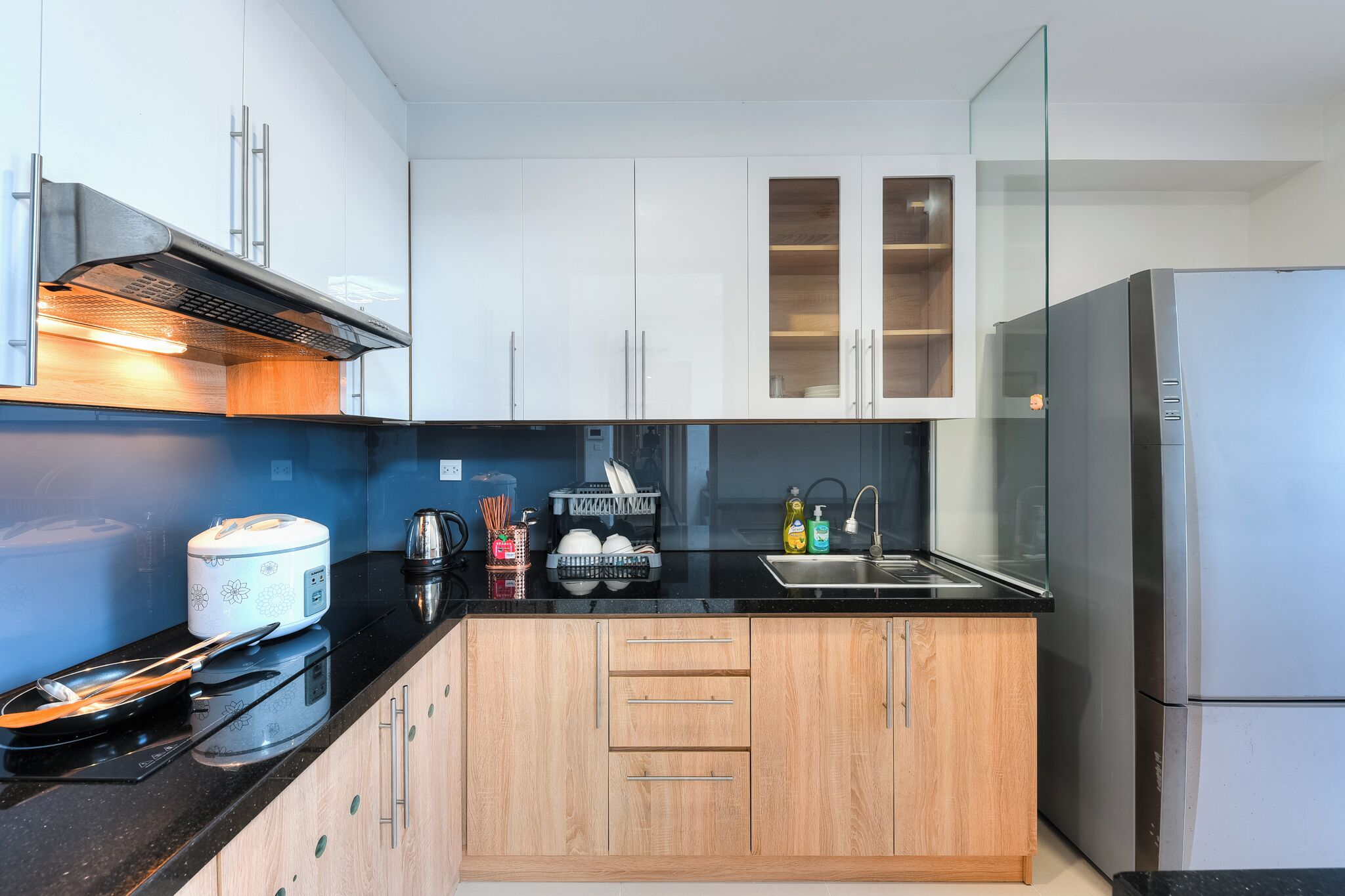 A modern kitchen with white cabinets, a black countertop, and a stainless steel refrigerator.