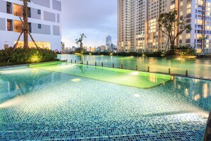 A swimming pool with clear blue tiles, surrounded by greenery and modern buildings. - REM Rivergate Garden Pool Signature Apartments (Ho Chi Minh City)