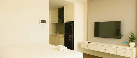 Habitación de hotel con cama, televisor montado en la pared, pequeña cocina y una mesita consola blanca.