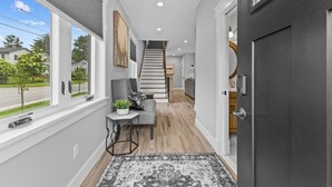 A hallway with a staircase, a gray armchair, a small table with a plant, and a patterned rug. - Enjoy Sunsets at Fully Equipped 4BR-Lake Champlain (Colchester)