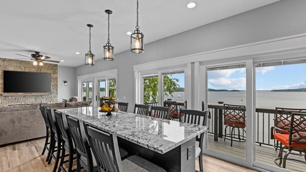 A spacious kitchen with a large island, modern pendant lights, and a view of a lake through large sliding doors. - Enjoy Sunsets at Fully Equipped 4BR-Lake Champlain (Colchester)