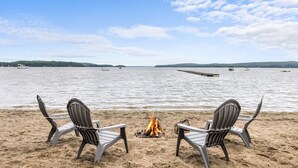 A beach with two Adirondack chairs facing a fire pit and a calm lake. - Enjoy Sunsets at Fully Equipped 4BR-Lake Champlain (Colchester)