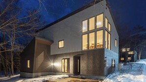 Una casa moderna de dos pisos con amplias ventanas y un exterior bien iluminado.