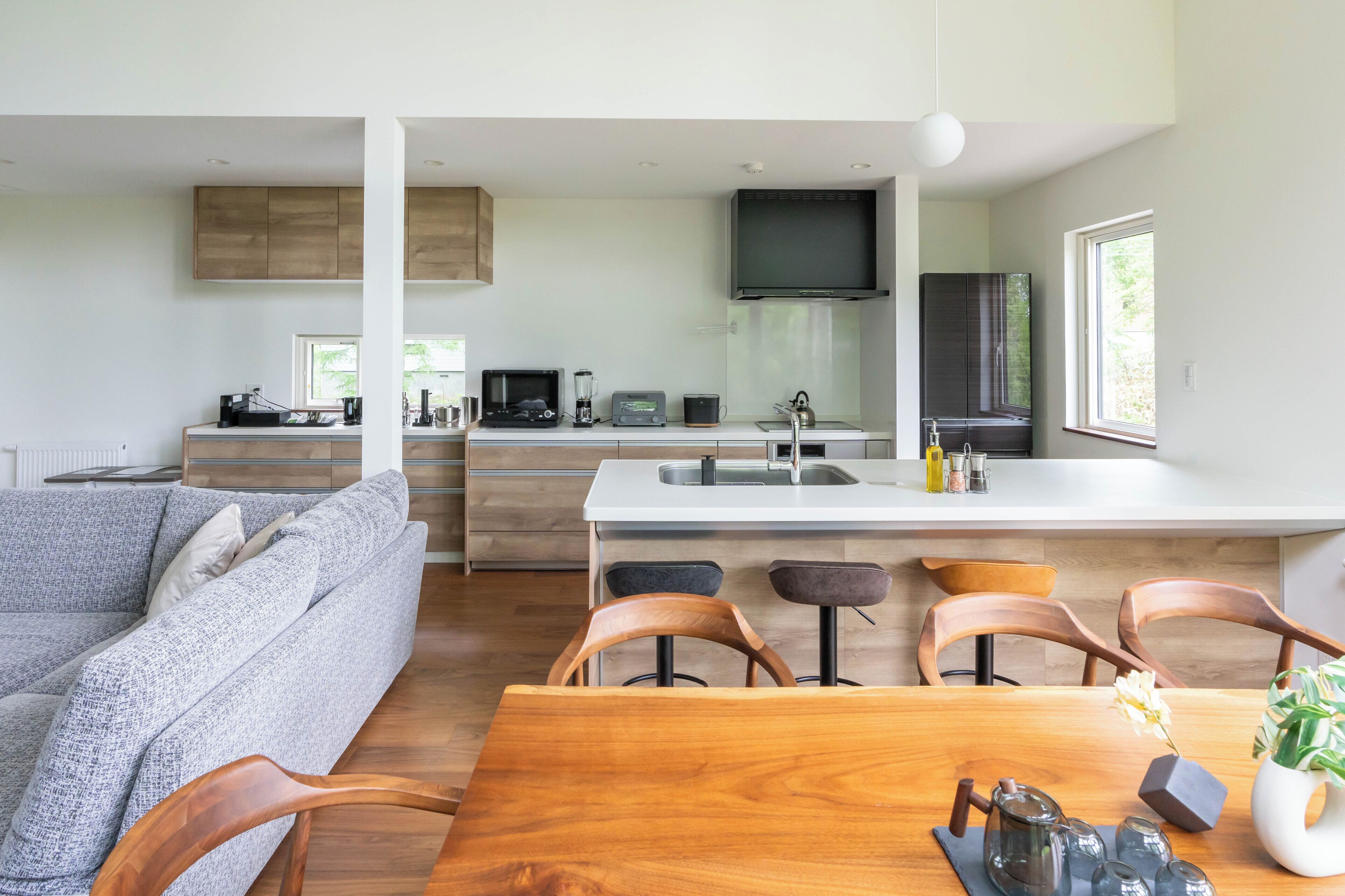A modern kitchen with a central island, a dining area with wooden chairs, and a grey sofa.