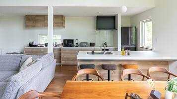 A modern kitchen with a central island, a dining area with wooden chairs, and a grey sofa.