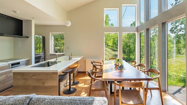 Cocina moderna con una isla central, mesa de comedor de madera y sillas, amplias ventanas con vistas a zonas verdes.