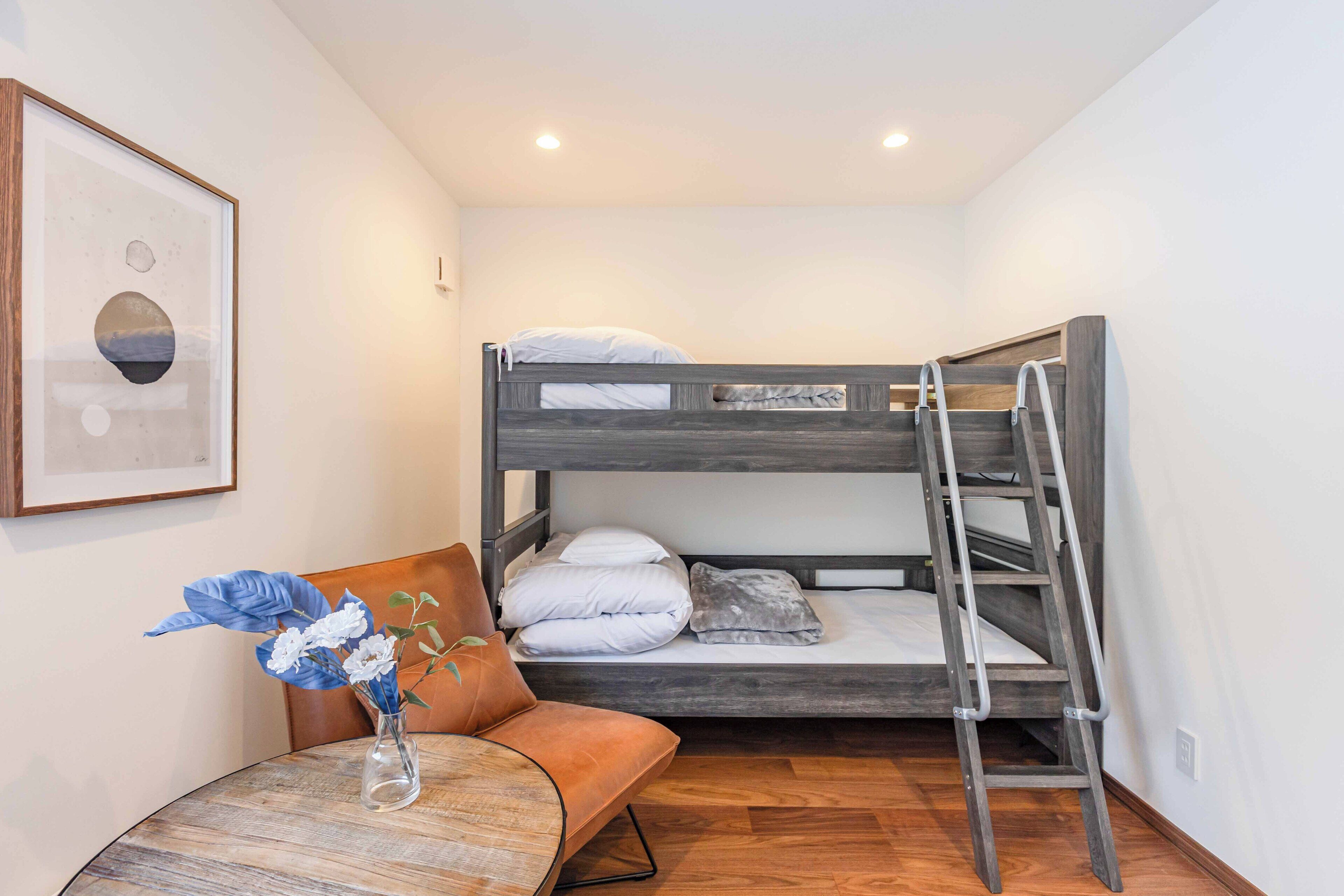 A bunk bed with a ladder, a small round table with a vase of flowers, and a framed picture on the wall.