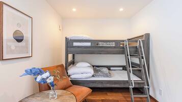 A bunk bed with a ladder, a small round table with a vase of flowers, and a framed picture on the wall.