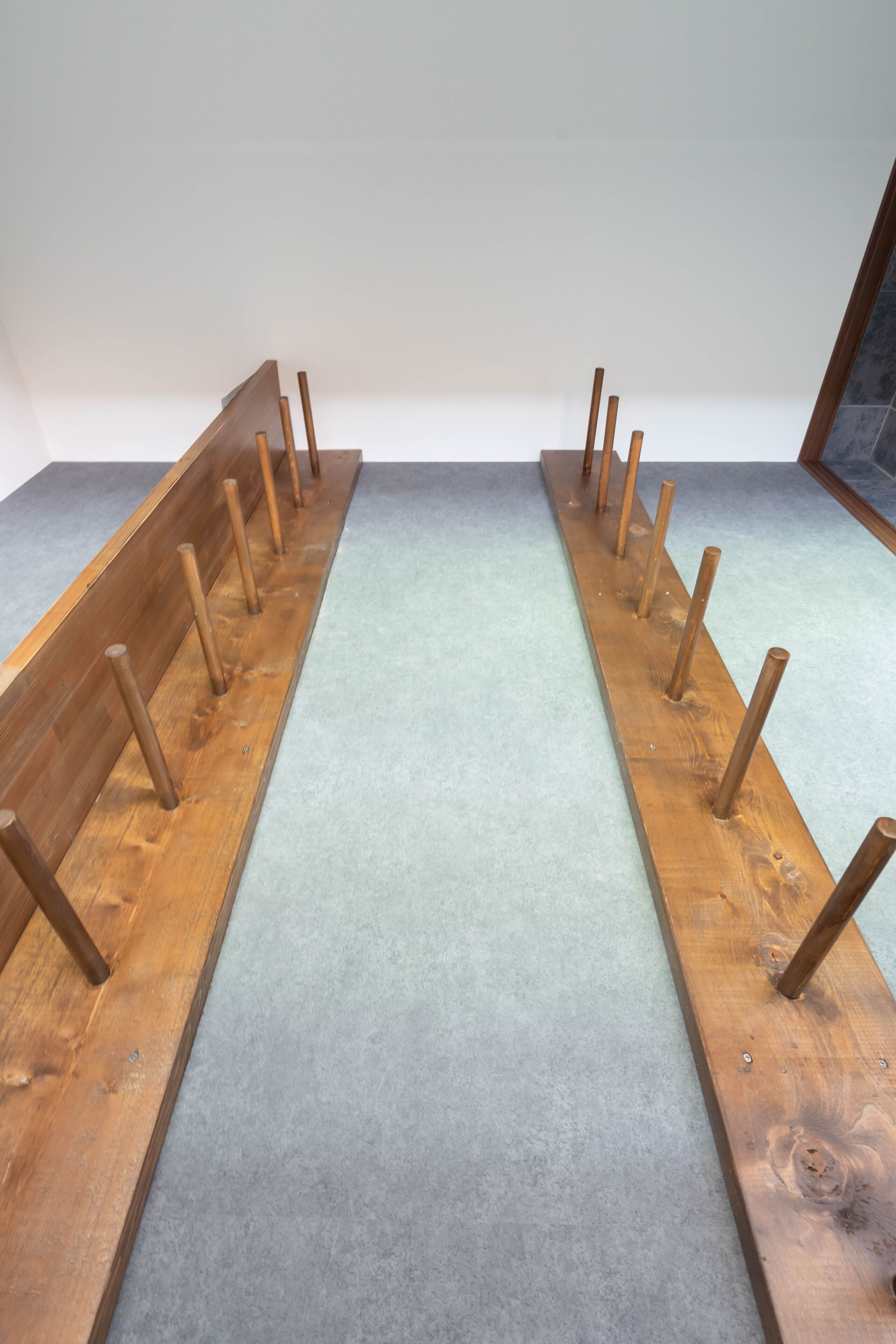 A wooden bench with multiple wooden poles in a room with a light-colored carpet.