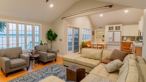 Un salon spacieux avec un plafond haut, un ventilateur de plafond et de grandes fenêtres donnant sur une étendue d’eau.