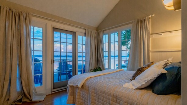Une chambre avec un grand lit, un ventilateur de plafond et une vue sur une étendue d’eau par les fenêtres.