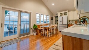 Une cuisine spacieuse dotée d’un plancher en bois, un coin repas avec une table et des chaises, et une vue sur un plan d’eau, accessible par de grandes portes-fenêtres coulissantes donnant sur un balcon.