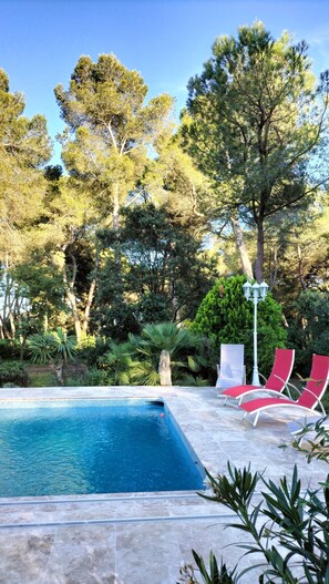 A swimming pool with red lounge chairs and a white lamp post.