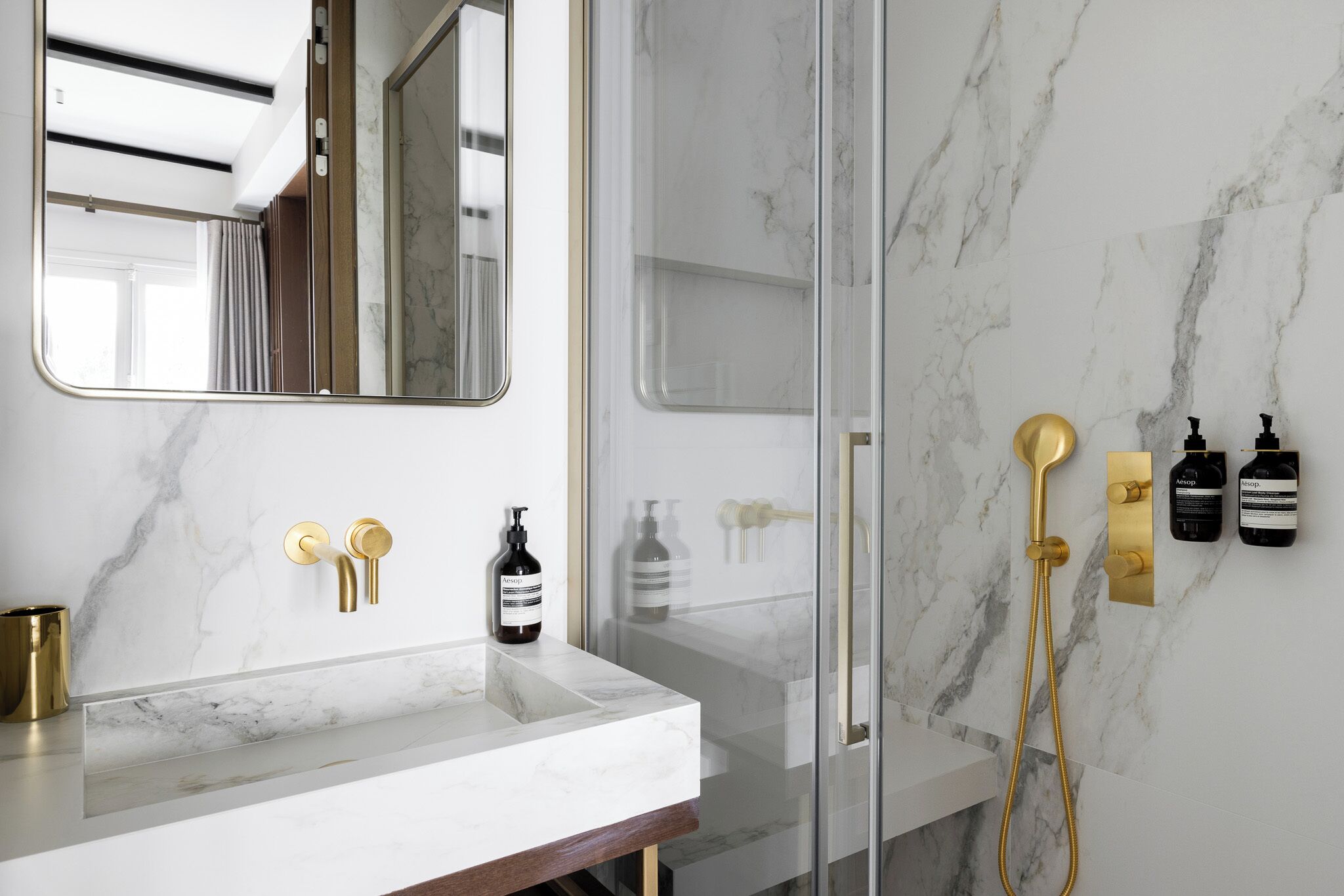 Une salle de bain moderne avec un comptoir en marbre, des accessoires dorés et une douche à l’italienne.