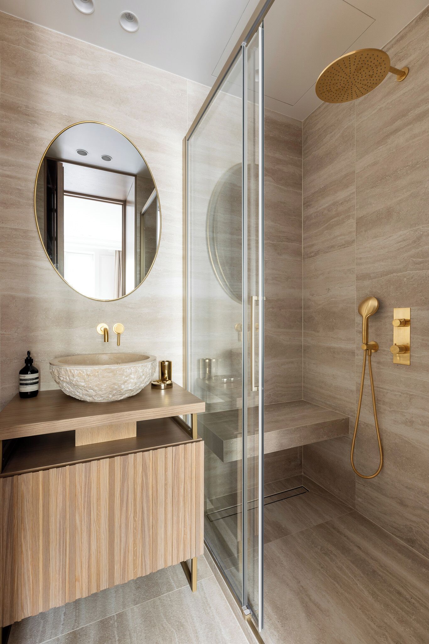 A modern bathroom with a glass shower enclosure, a round mirror, and a wooden vanity.